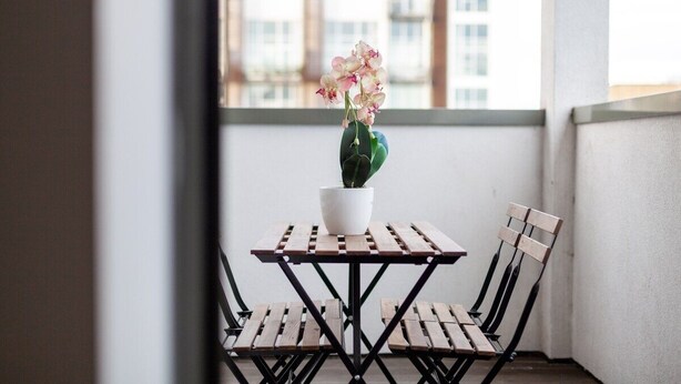 A small balcony with a wooden table and two chairs, a potted plant, and a view of buildings. - Luxury Studios | E8 4DN | Balcony (London)