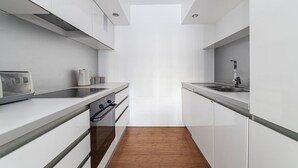 A narrow kitchen with white cabinets, a built-in oven, and a microwave. - Luxury Studios | E8 4DN | Balcony (London)