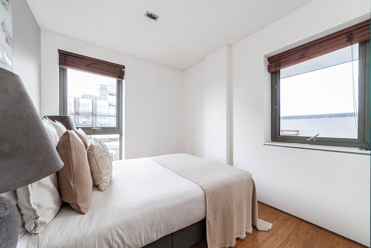 Une chambre à coucher avec un lit, deux fenêtres équipées de stores, une vue sur la ville et un plancher en bois.