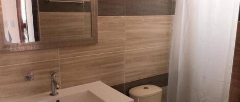 A bathroom with a sink, mirror, toilet, and shower curtain.