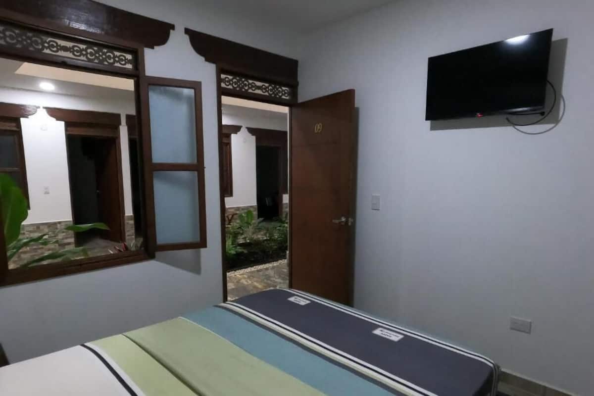 A room with a bed, a TV mounted on the wall, and a door leading to another room.
