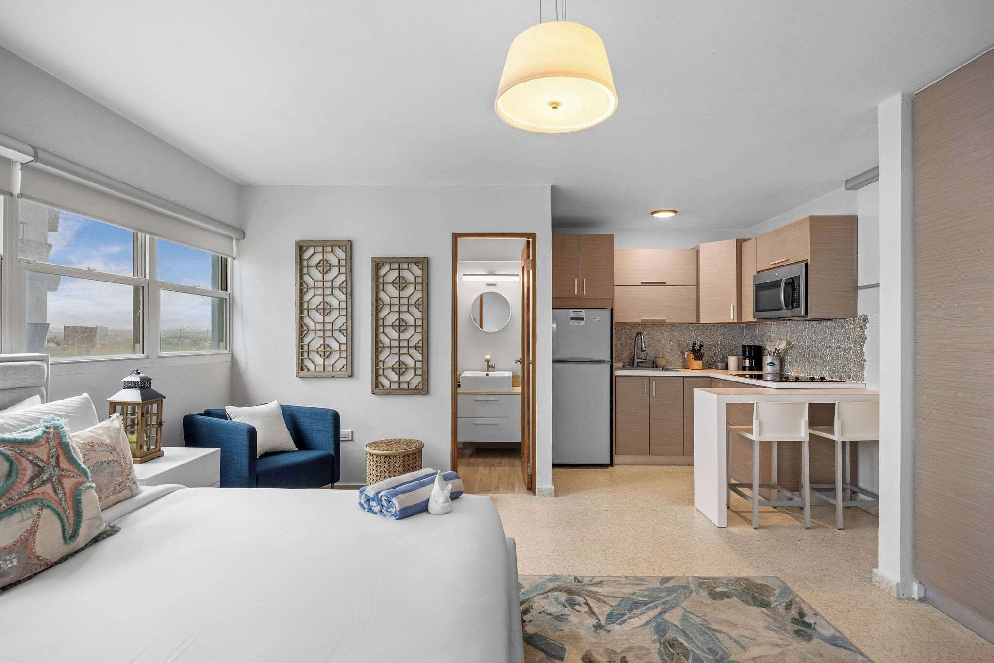 Una habitación de hotel moderna con cama, escritorio, kitchenette y baño.