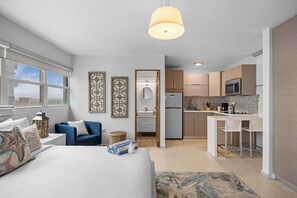 A modern hotel room with a bed, a desk, a kitchenette, and a bathroom. - Atlantic Studio | Beachfront Location (Carolina)