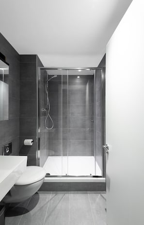 Une salle de bain moderne dotée d’une douche à parois de verre, de toilettes et d’un lavabo.