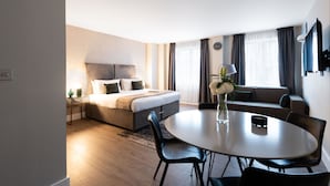 Una habitación de hotel moderna con una cama, un sofá, una mesa de comedor con sillas y un televisor montado en la pared.