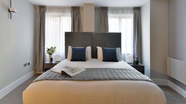 Una habitación de hotel moderna con una cama grande, dos mesitas de noche, una lámpara de pared y vistas a la ciudad.