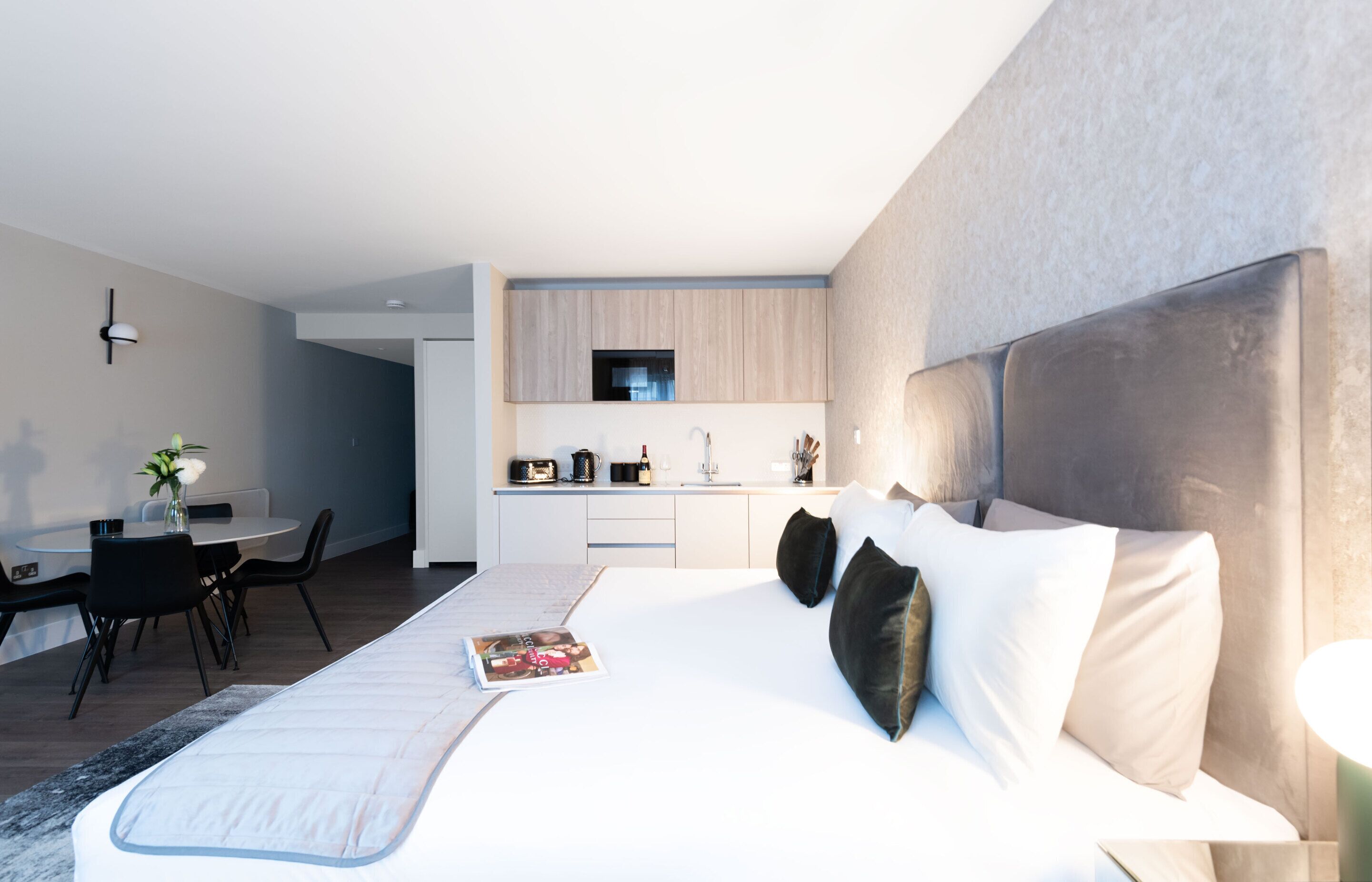 A modern hotel room with a large bed, a dining area, and a kitchenette.
