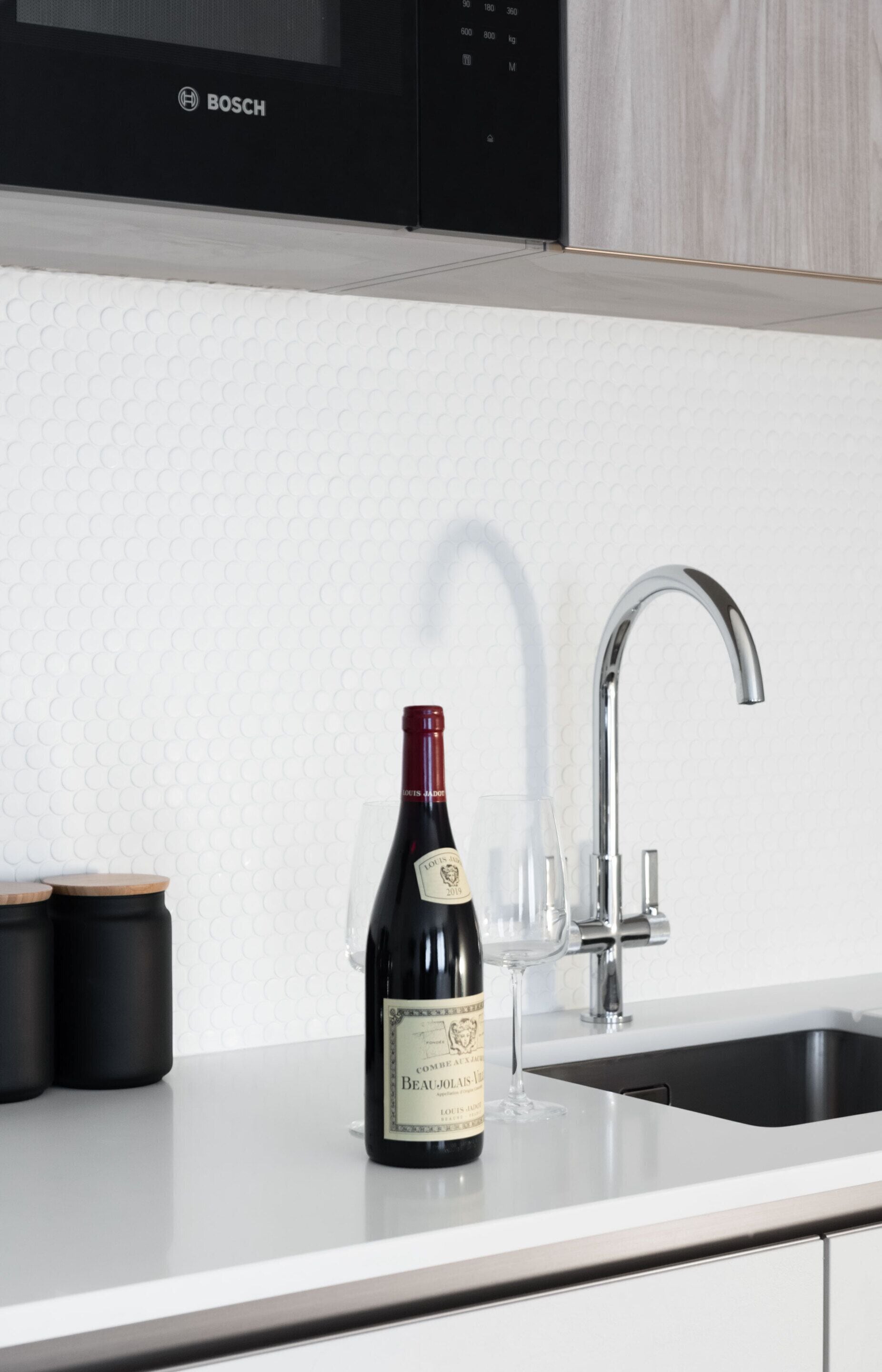 A kitchen with a Bosch microwave, a wine bottle, and a wine glass on the counter.