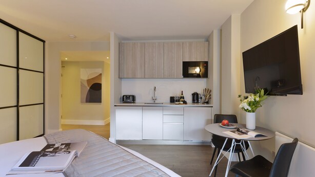 A modern hotel room with a bed, a small dining table with chairs, a kitchen area with a TV, and a bathroom visible in the background. - Studio near Oxford Street (London)
