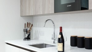 A modern kitchen with white cabinets, a Bosch microwave, a stainless steel sink, and a wine bottle. - Studio near Oxford Street (London)