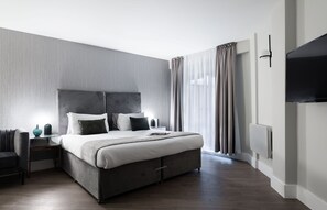 A modern hotel room with a large bed, a flat-screen TV, and a bedside table with a lamp. - Studio near Oxford Street (London)
