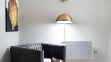 A modern living room with a dark sofa, a floor lamp, and a wall-mounted speaker.