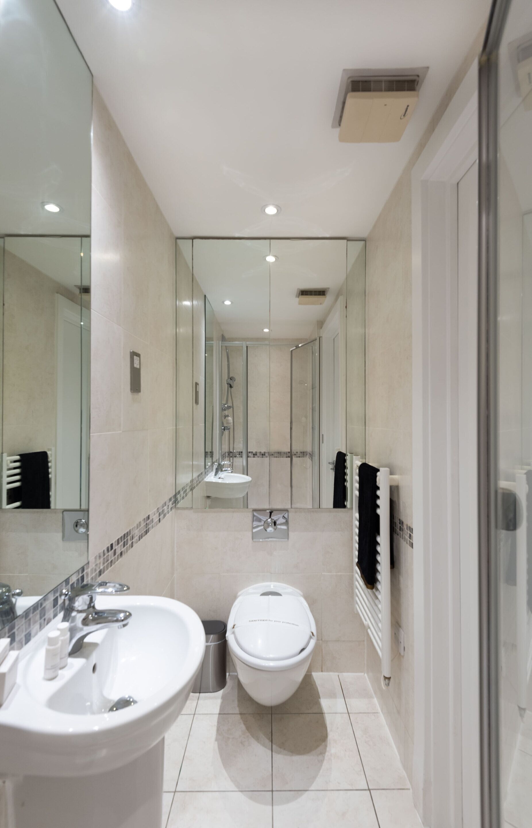 A modern bathroom with a large mirror, a sink, a toilet, and a shower area.