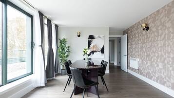 Un espace repas moderne avec une table ronde, des chaises noires, un vase de fleurs et une grande fenêtre avec des rideaux.
