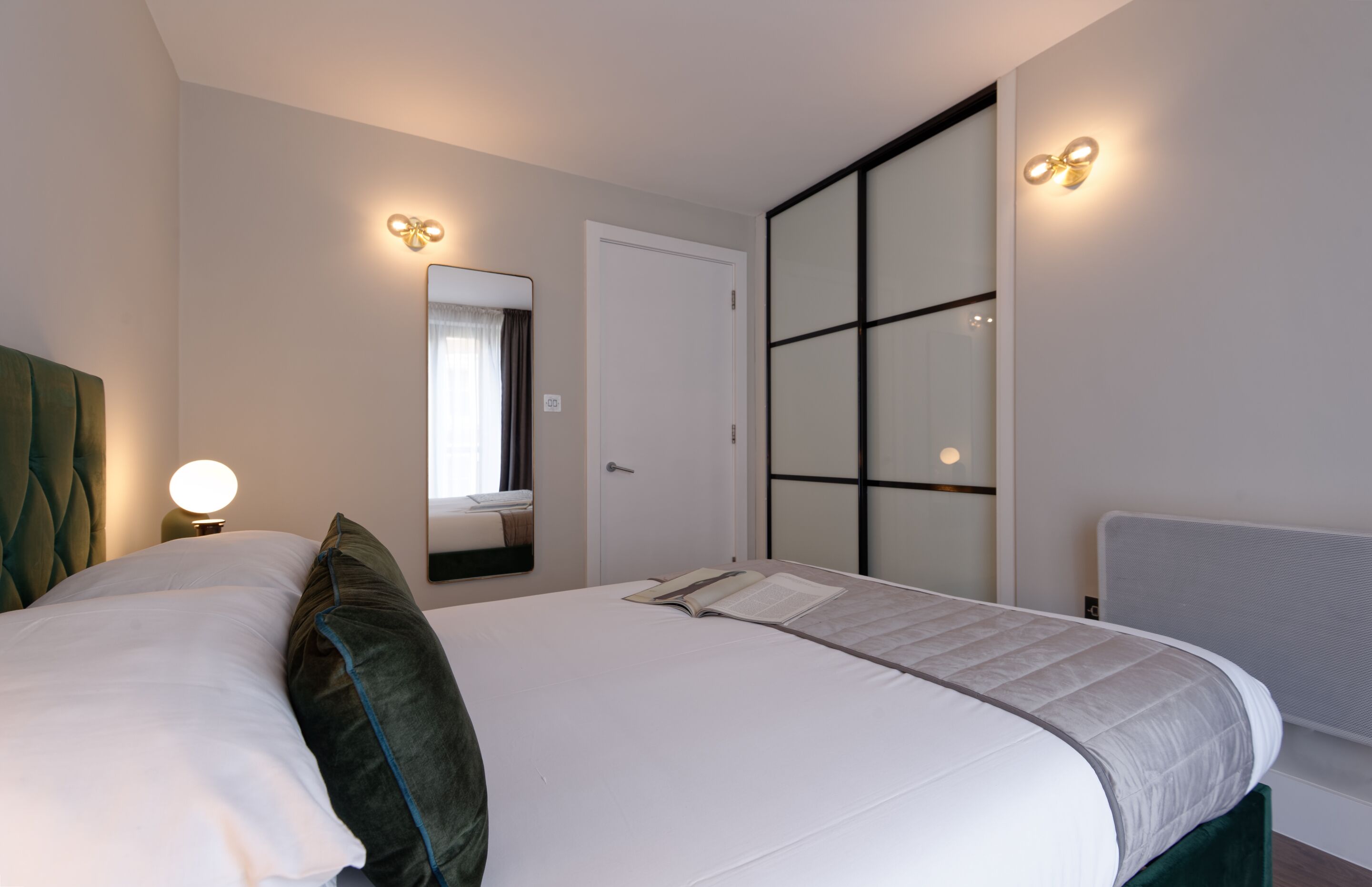 Une chambre d’hôtel moderne avec un grand lit, une table de chevet avec une lampe, un miroir et une porte coulissante.