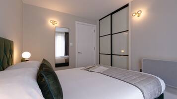 Une chambre d’hôtel moderne avec un grand lit, une table de chevet avec une lampe, un miroir et une porte coulissante.