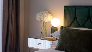 En pænt redt seng med et grønt sengegærde, et natbord med en vase blomster, en lampe og en bog.
