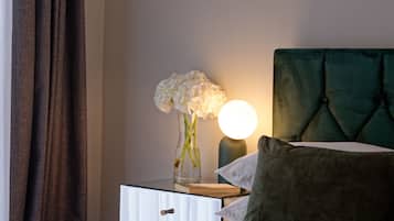 A neatly made bed with a green headboard, a bedside table with a vase of flowers, a lamp, and a book.