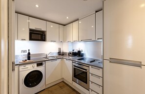Une cuisine compacte avec des meubles blancs, un four à micro-ondes encastré, un lave-linge et une cuisinière.