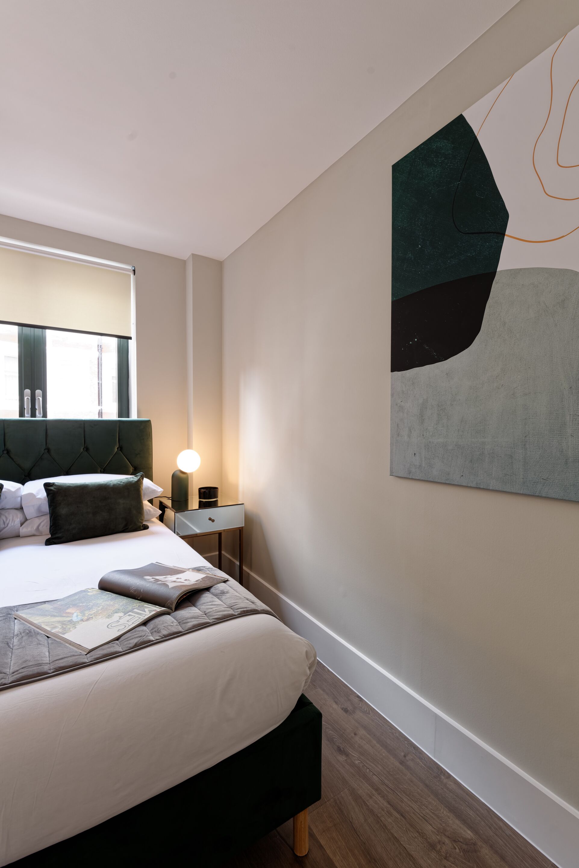 A modern bedroom with a large bed, a bedside table with a lamp, and a wall-mounted abstract painting.