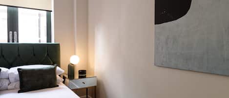 A modern bedroom with a large bed, a bedside table with a lamp, and a wall-mounted abstract painting.