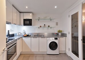 A compact kitchen with a built-in microwave, a washing machine, and a toaster. - Two-Bedroom Apartment near Oxford Street (London)
