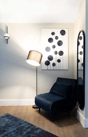 A modern room with a dark blue armchair, a floor lamp, a wall-mounted mirror, and a piece of abstract art. - Two-Bedroom Apartment near Oxford Street (London)