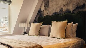 Une chambre d’hôtel avec un lit, des oreillers, une lampe et une vue sur les bâtiments par la fenêtre.