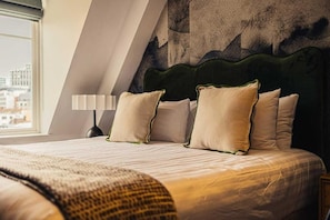 Une chambre d’hôtel avec un lit, des oreillers, une lampe et une vue sur les bâtiments par la fenêtre.