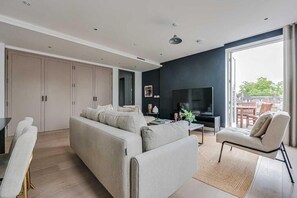 A modern living room with a sofa, a TV, a coffee table, and a chair. There is a sliding door leading to an outdoor area.