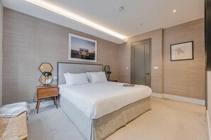 A modern bedroom with a large bed, a nightstand, a lamp, and a framed picture on the wall.
