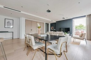 Ein modernes Wohnzimmer mit Essbereich, einer Sofagarnitur, einem Fernseher und einem großen Fenster.