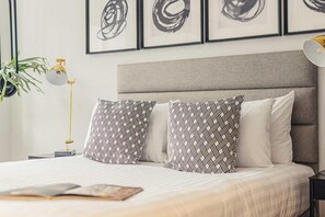 Een opgemaakt bed met gestreepte kussens, een bedlamp en een lijst met kunst aan de muur.