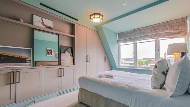 A bedroom with a bed, a window with a view, and built-in storage. - Three-Bedroom Duplex Penthouse (London)