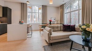 A modern living room with a sofa, a dining table, and a kitchen area. - Three-Bedroom Duplex Penthouse (London)