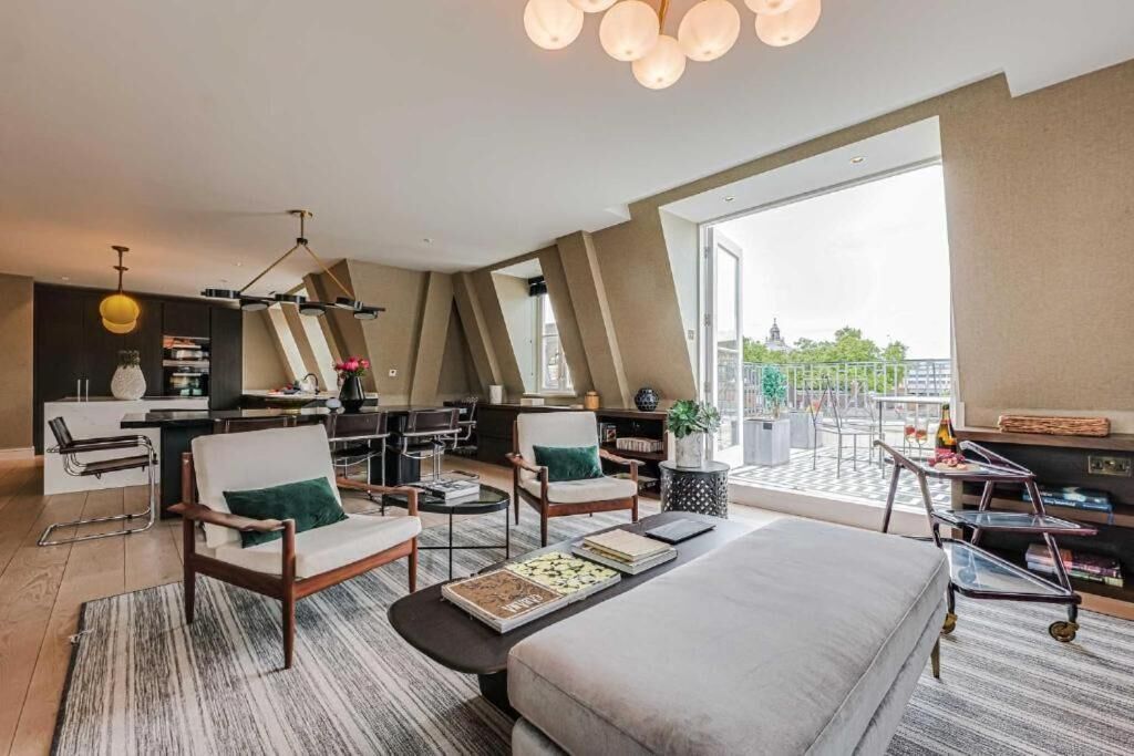 A modern hotel room with a large bed, two armchairs, a desk, and a balcony with a view.