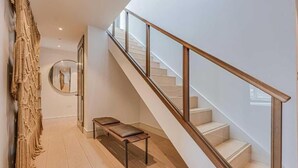 A modern interior with a staircase, a bench, and a wall-mounted mirror. - Three-Bedroom Duplex Penthouse (London)