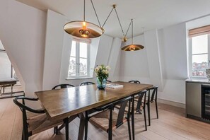 A dining area with a wooden table, black chairs, and pendant lighting. - Three-Bedroom Duplex Penthouse (London)