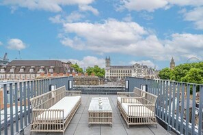 Une terrasse sur le toit, meublée de mobilier en osier, offrant une vue sur des bâtiments historiques et un ciel dégagé.