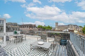 A rooftop terrace with a chevron-patterned floor, outdoor seating, and a view of historic buildings including a tower. - Three-Bedroom Duplex Penthouse (London)