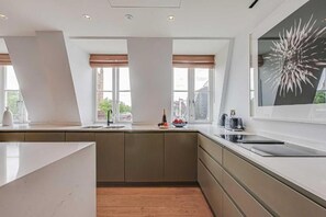A modern kitchen with a large island, a built-in oven, and a view of the city. - Three-Bedroom Duplex Penthouse (London)