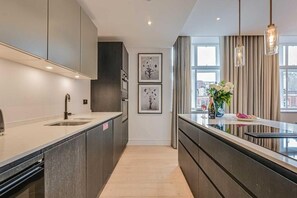 Een moderne keuken met een centraal eiland, hanglampen en een gekaderd kunstwerk aan de muur.