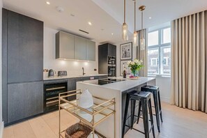 A modern kitchen with a central island, bar stools, and pendant lighting. - Three-Bedroom Superior Apartment (London)