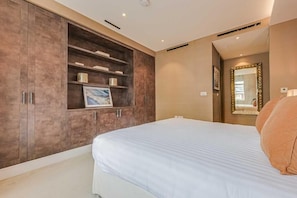 Een slaapkamer met een groot bed, een inbouwledingkast van hout en een spiegel met decoratieve verlichting.