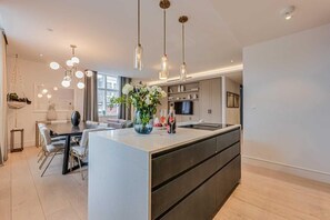 Een moderne keuken met een centraal eiland, hangende lampen en een zithoek met een bank.