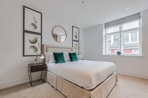 A bedroom with a bed, bedside table, lamp, and framed artwork on the wall. - Three-Bedroom Superior Apartment (London)