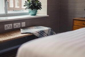 Ein Zimmer mit Fensterbank, einem Blumentopf, einer Bank und einem Nachttisch.