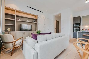 Ein modernes Wohnzimmer mit Sofa, Sesseln, Fernseher und Küchenzeile.