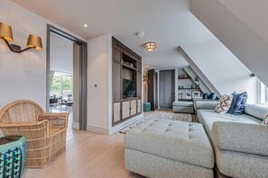 Ein modernes Wohnzimmer mit einer Couch, einem Korbsessel, einem Schrank und einem Fernseher.