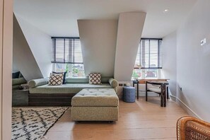 A loft-style bedroom with a built-in sofa, ottoman, and a small table. - Four Bedroom Duplex Penthouse (London)